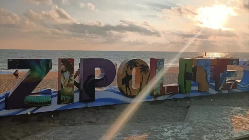 The large block letters of the Zipolite sign with the setting sun behind them over the sea.