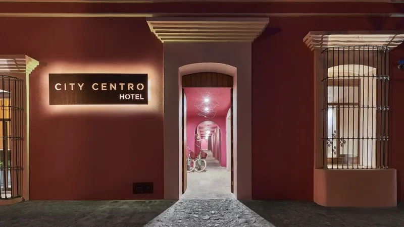Image of the entrance of the Hotel City Centro in Oaxaca, showcasing its bright pink sign and walls.