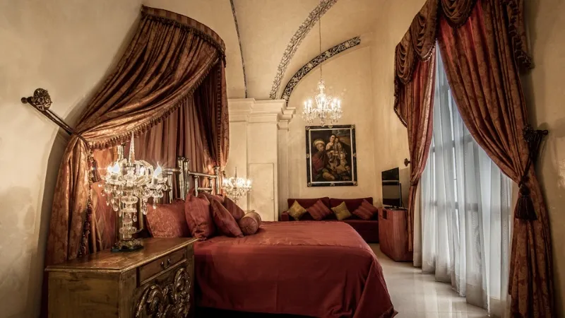 Image of a bedroom in the Hotel Palacio Borghese in Oaxaca, taken from the right side of the bed, with an image on the wall in the background to the right