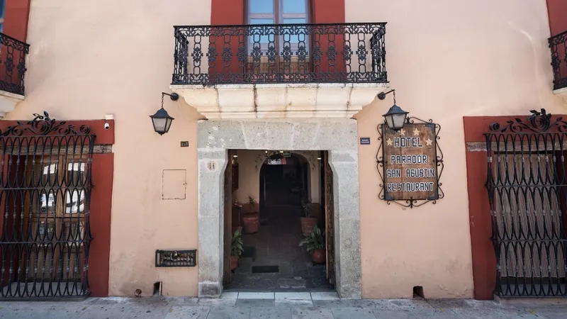 The front entrance of Hotel Parador San Agustín taken from the street.  The sign of the hotel is affixed to the wall on the right side of the entrance.