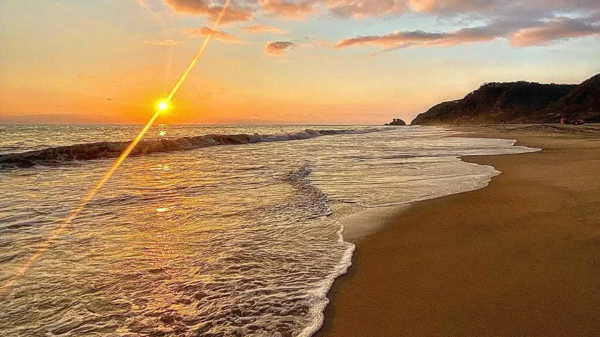 Playa Mermejita in Mazunte, taken with the sands of the beach on the right, the lapping waves on the left, and the setting sun on the horizon