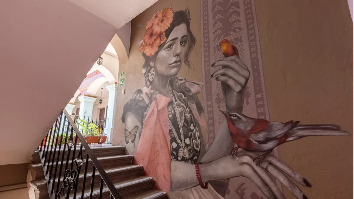 Painting of a smiling woman with a bird perched on her hand on an interior stairwell wall at Selina Oaxaca
