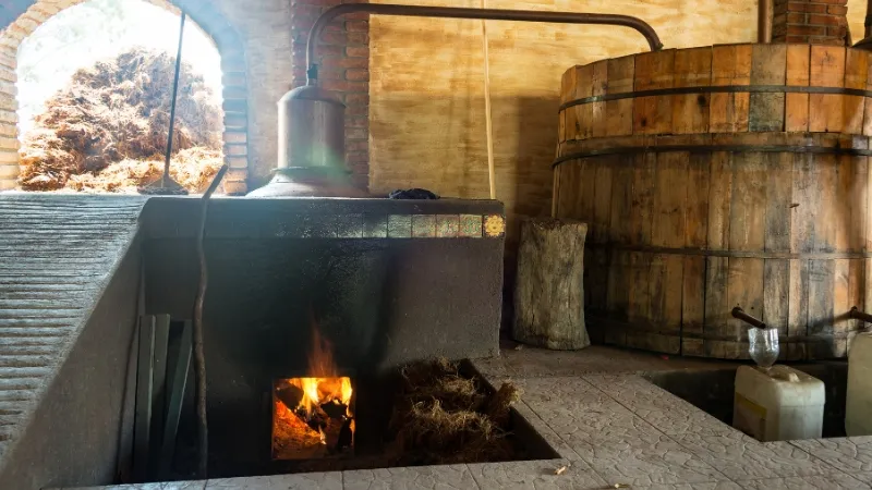 A small artesanal mezcal production center with a wood-fire heated distillation unit and large wooden storage vat 